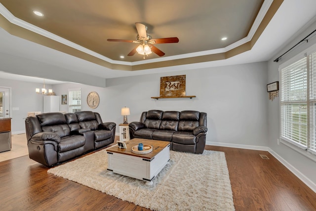 living room featuring a tray ceiling, hardwood / wood-style floors, ceiling fan with notable chandelier, and crown molding