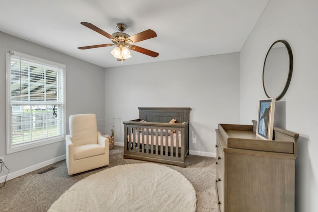 bedroom featuring a nursery area, carpet floors, and ceiling fan