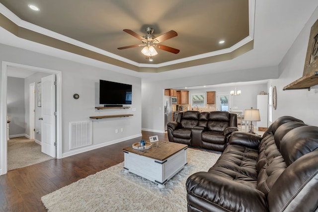 living room featuring a tray ceiling, wood-type flooring, ornamental molding, and ceiling fan with notable chandelier