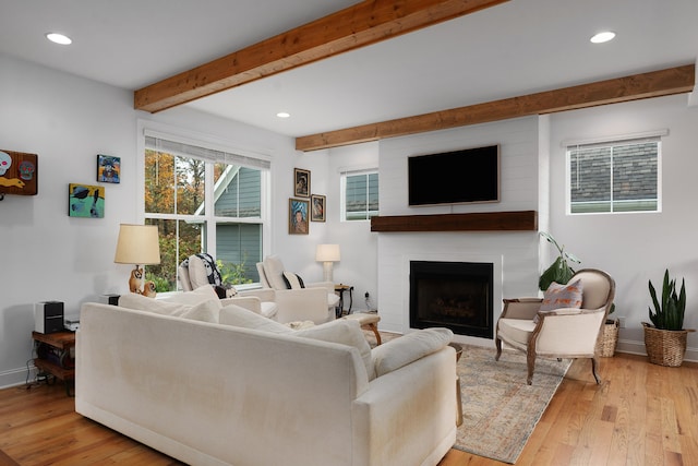 living room featuring light hardwood / wood-style floors, beam ceiling, and a large fireplace