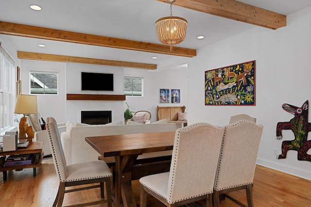 dining area featuring beamed ceiling, an inviting chandelier, wood-type flooring, and a large fireplace