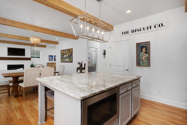 kitchen featuring a center island, stainless steel microwave, a kitchen breakfast bar, pendant lighting, and light hardwood / wood-style flooring