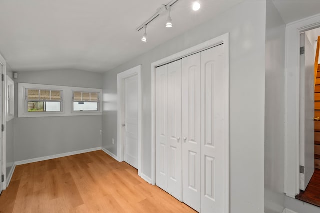 unfurnished bedroom featuring rail lighting, a closet, light hardwood / wood-style flooring, and lofted ceiling