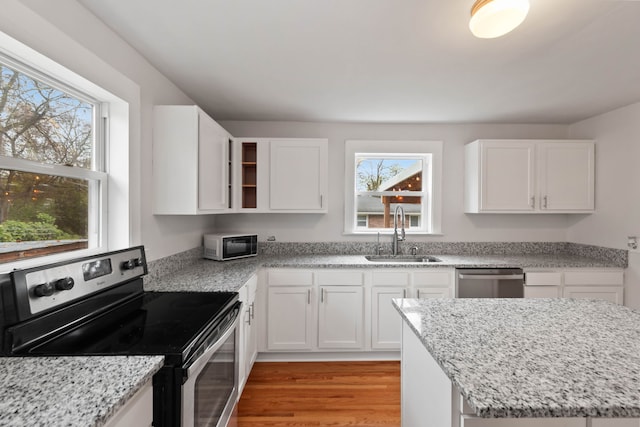 kitchen with sink, light stone counters, appliances with stainless steel finishes, white cabinets, and light wood-type flooring