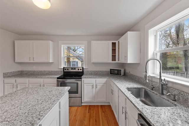 kitchen with sink, light stone countertops, light hardwood / wood-style flooring, white cabinets, and electric range