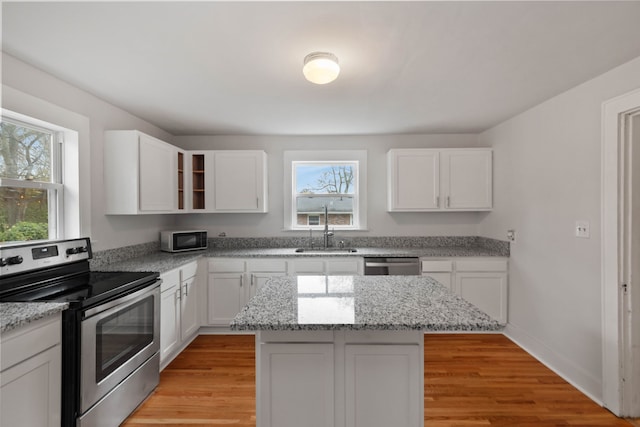 kitchen with sink, appliances with stainless steel finishes, a kitchen island, white cabinets, and light wood-type flooring