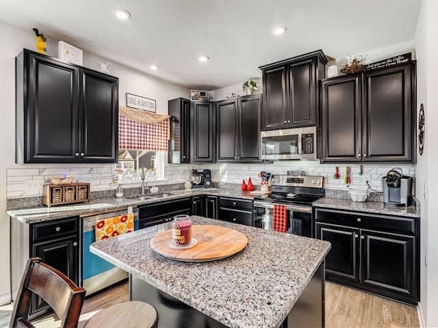 kitchen featuring light stone counters, appliances with stainless steel finishes, sink, light hardwood / wood-style floors, and a center island