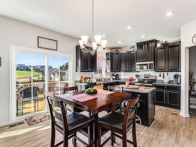 kitchen featuring light stone counters, stainless steel appliances, decorative light fixtures, decorative backsplash, and light hardwood / wood-style floors