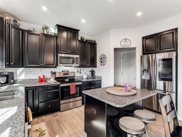 kitchen with stainless steel appliances, backsplash, a kitchen bar, light stone countertops, and light hardwood / wood-style floors