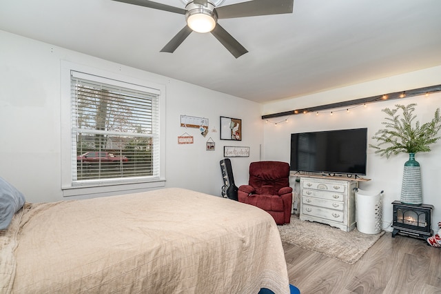 bedroom featuring a wood stove, ceiling fan, and wood-type flooring