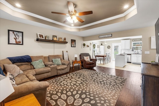 living room featuring sink, ceiling fan, crown molding, a tray ceiling, and light hardwood / wood-style flooring