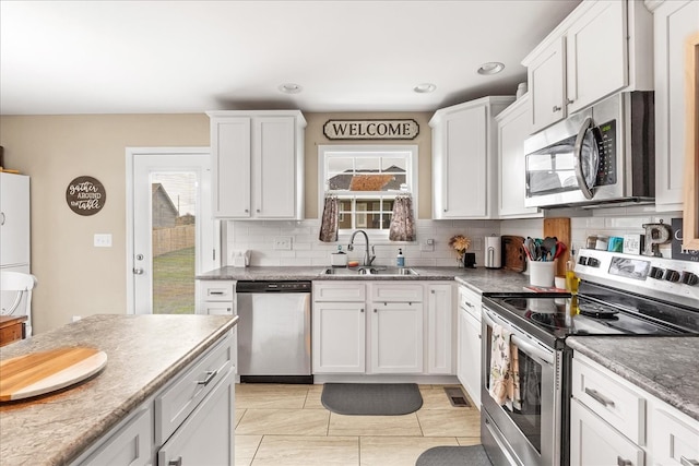 kitchen with stainless steel appliances, light tile patterned flooring, white cabinetry, sink, and decorative backsplash