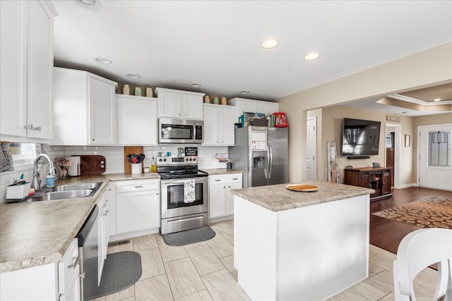 kitchen featuring stainless steel appliances, white cabinetry, sink, tasteful backsplash, and a center island