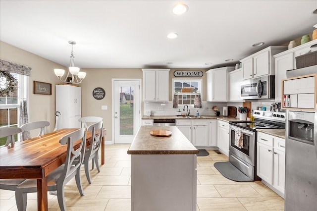 kitchen featuring appliances with stainless steel finishes, decorative light fixtures, a chandelier, a center island, and white cabinets