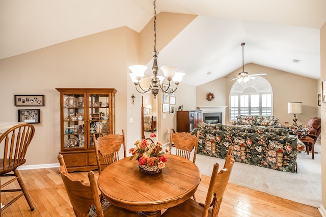 dining room featuring light hardwood / wood-style floors, ceiling fan with notable chandelier, and vaulted ceiling