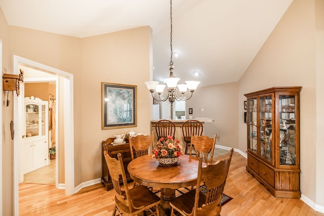 dining room with light wood-type flooring, an inviting chandelier, and vaulted ceiling