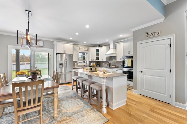 kitchen with light hardwood / wood-style floors, light stone counters, white cabinets, appliances with stainless steel finishes, and decorative light fixtures