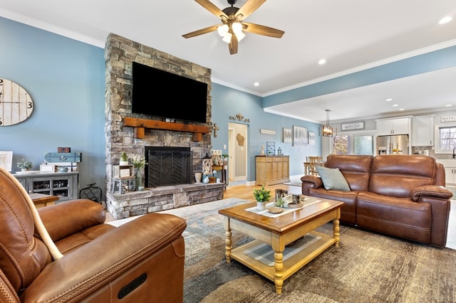 living room with a stone fireplace, ceiling fan, wood-type flooring, and ornamental molding