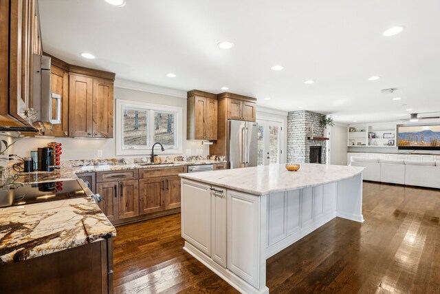 kitchen with light stone counters, stainless steel appliances, dark wood-type flooring, sink, and a kitchen island