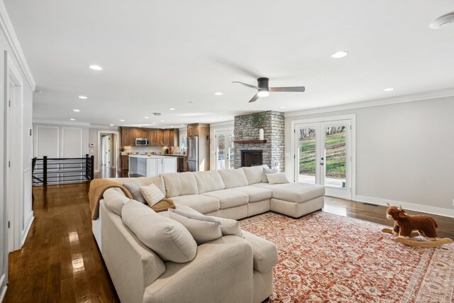 living room with ceiling fan, french doors, a large fireplace, dark hardwood / wood-style floors, and crown molding