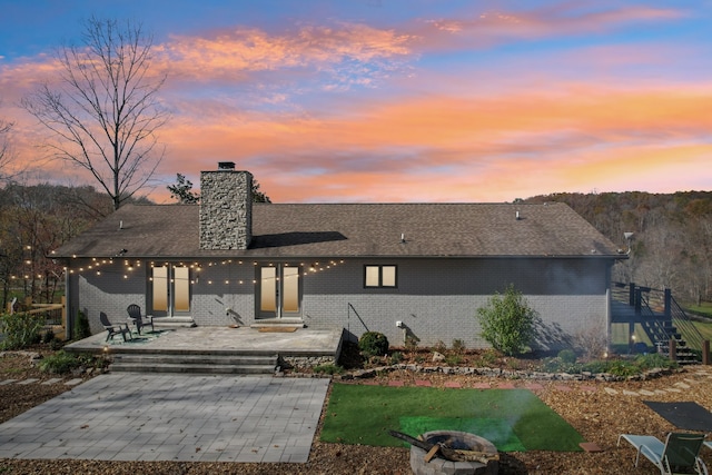 back house at dusk featuring a patio and an outdoor fire pit