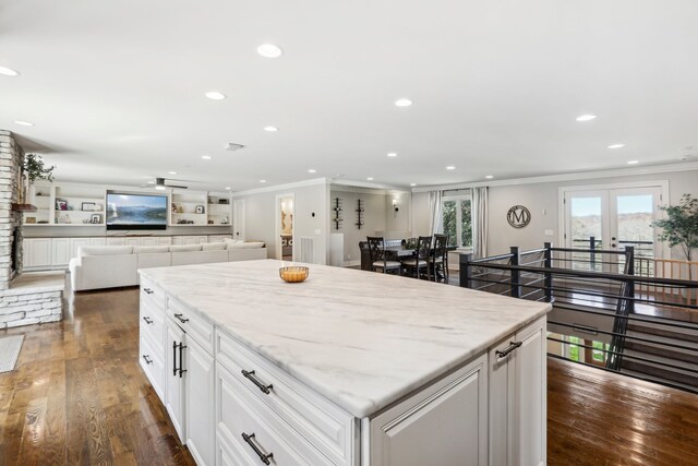 kitchen featuring light stone countertops, ornamental molding, dark wood-type flooring, white cabinetry, and a kitchen island