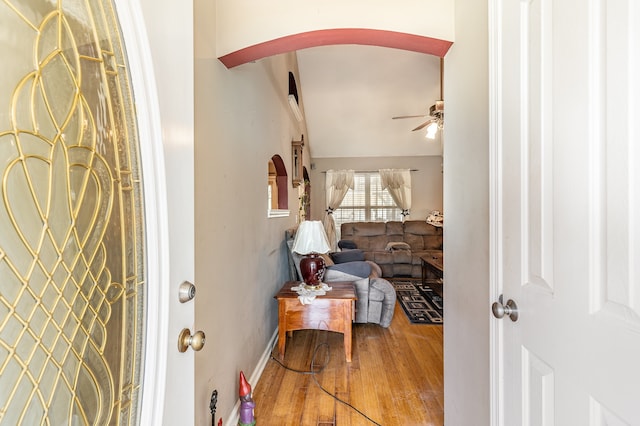 foyer with arched walkways, wood finished floors, a ceiling fan, baseboards, and vaulted ceiling