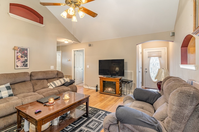 living area with arched walkways, a glass covered fireplace, ceiling fan, wood finished floors, and high vaulted ceiling