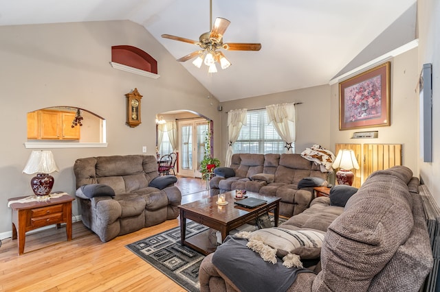 living room with light wood-type flooring, high vaulted ceiling, ceiling fan, and arched walkways