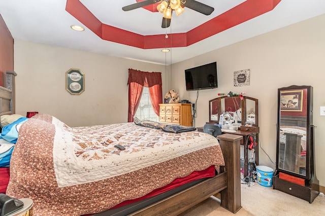 bedroom with ceiling fan, a tray ceiling, and light colored carpet