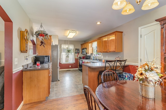 kitchen featuring dark countertops, brown cabinetry, a sink, a peninsula, and black appliances