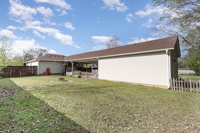 rear view of property with a yard, an outdoor fire pit, and fence