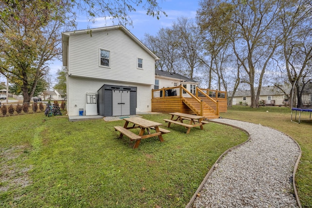 back of property featuring a wooden deck, a trampoline, and a lawn