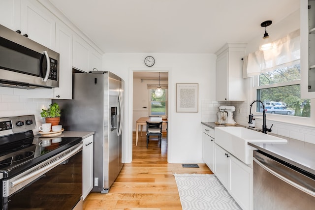 kitchen with pendant lighting, light wood-type flooring, stainless steel appliances, and white cabinetry