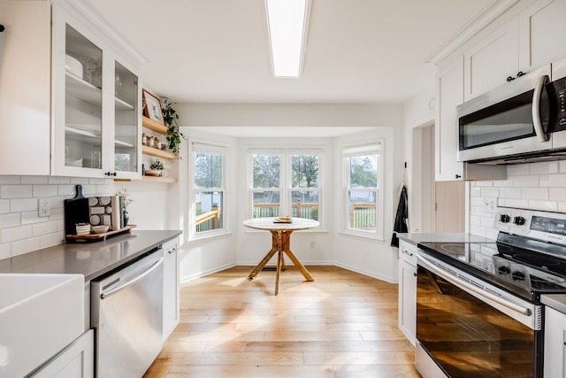 kitchen with white cabinets, appliances with stainless steel finishes, light hardwood / wood-style floors, and backsplash