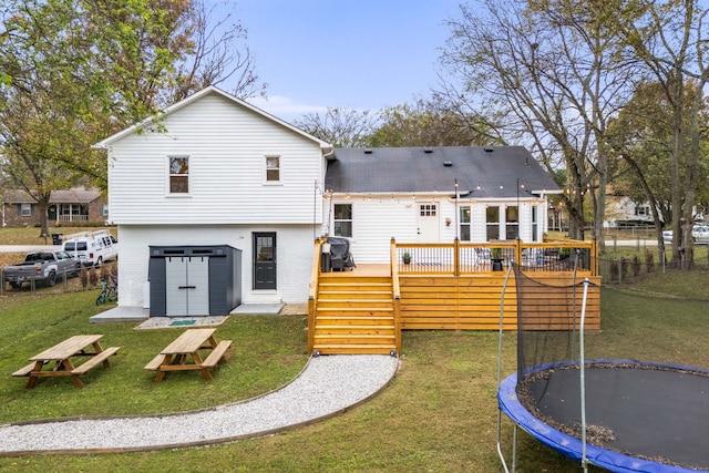 rear view of house featuring a lawn, a wooden deck, and a trampoline