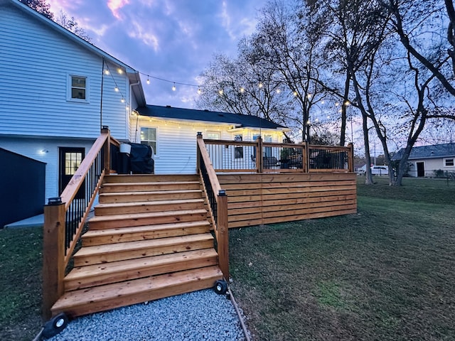 back house at dusk featuring a lawn and a deck