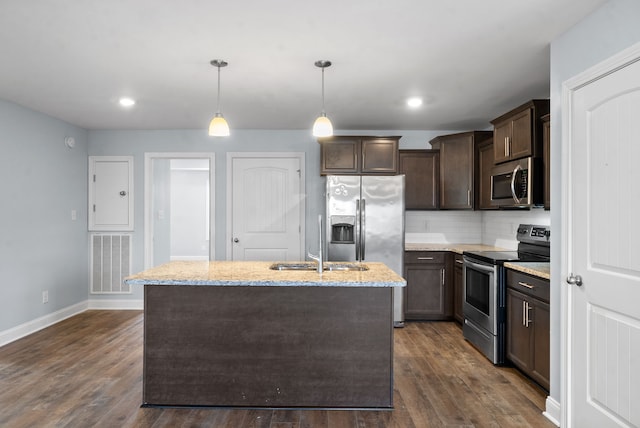 kitchen featuring a center island with sink, light stone counters, appliances with stainless steel finishes, hanging light fixtures, and dark hardwood / wood-style flooring