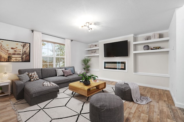 living room featuring built in shelves, light wood-type flooring, and a textured ceiling