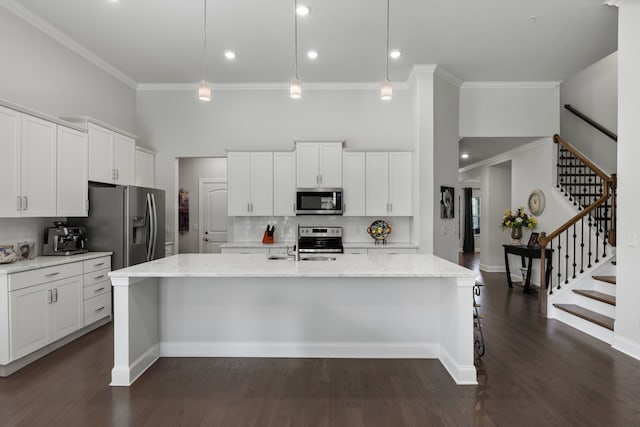 kitchen with pendant lighting, appliances with stainless steel finishes, dark wood-type flooring, and a center island with sink