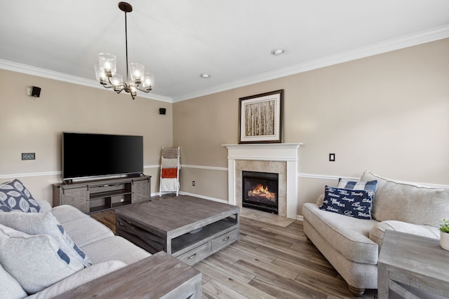 living room featuring a tiled fireplace, light hardwood / wood-style floors, a notable chandelier, and crown molding