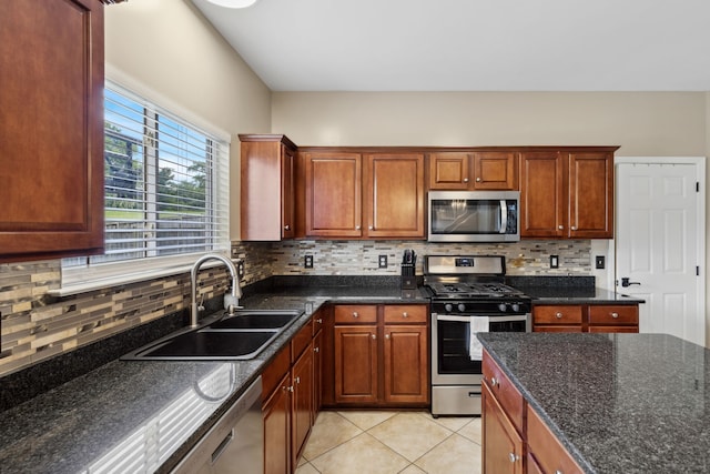 kitchen with decorative backsplash, sink, light tile patterned floors, appliances with stainless steel finishes, and dark stone countertops