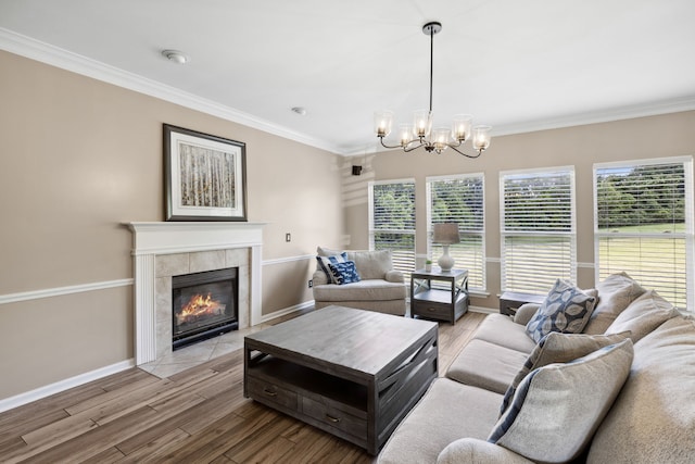 living room featuring light wood-type flooring, a tile fireplace, ornamental molding, and a notable chandelier