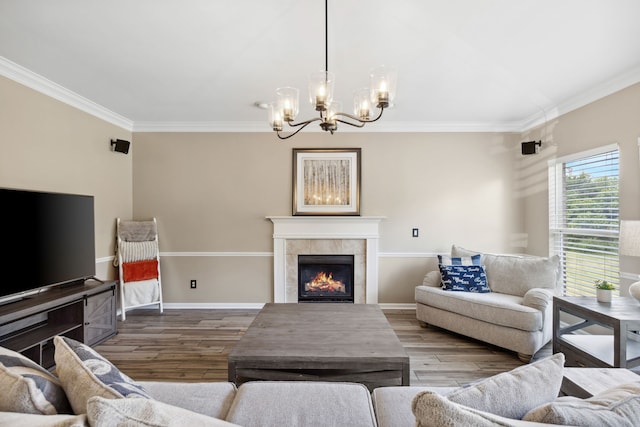 living room featuring wood-type flooring, an inviting chandelier, a tiled fireplace, and ornamental molding