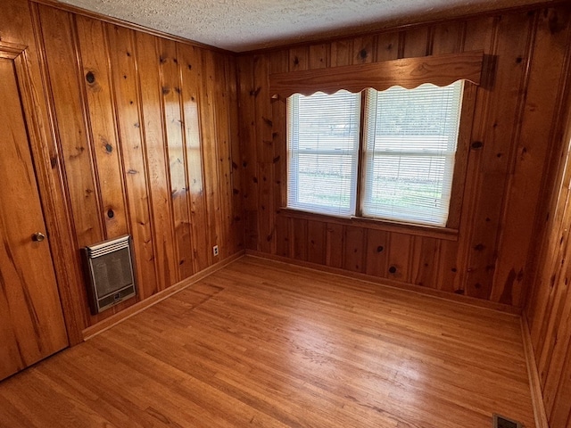 empty room featuring light wood-type flooring, wooden walls, and heating unit