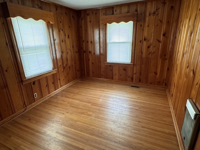 unfurnished room with light wood-type flooring and wooden walls