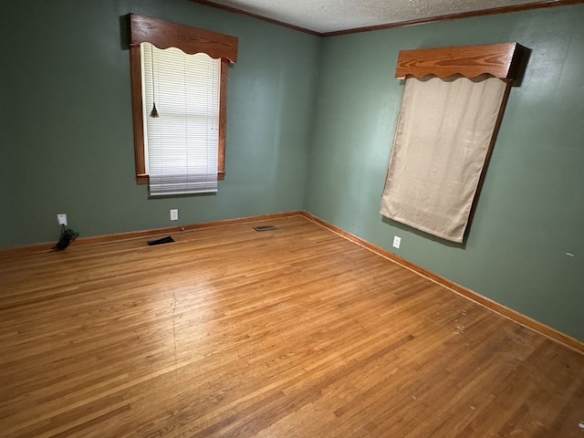 empty room featuring a textured ceiling, light wood-type flooring, and ornamental molding