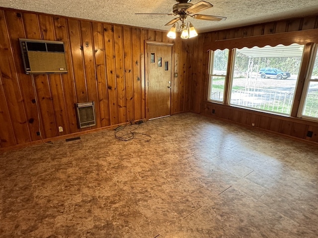 empty room with wood walls, a wealth of natural light, a textured ceiling, and ceiling fan