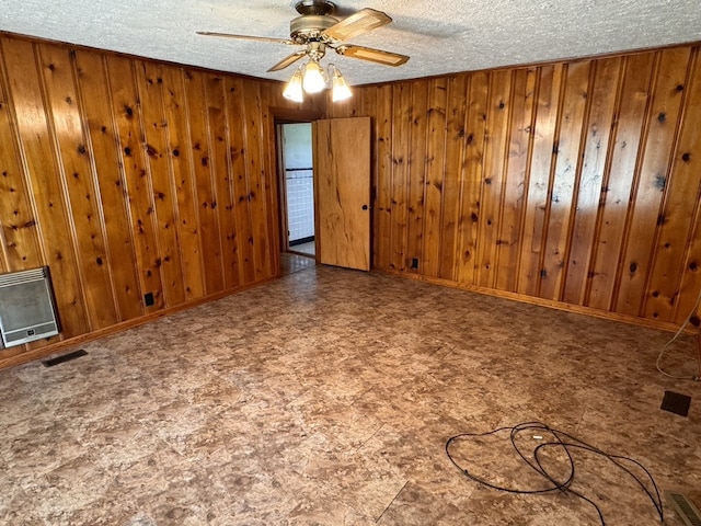 unfurnished living room with wood walls, a textured ceiling, ceiling fan, and heating unit