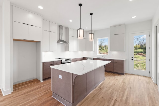 kitchen featuring pendant lighting, sink, light hardwood / wood-style flooring, wall chimney exhaust hood, and a kitchen island